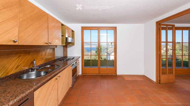 Modern kitchen with wooden cabinets, granite countertop, stainless steel sink, and built-in oven. Features large wooden sliding doors leading to a scenic view.