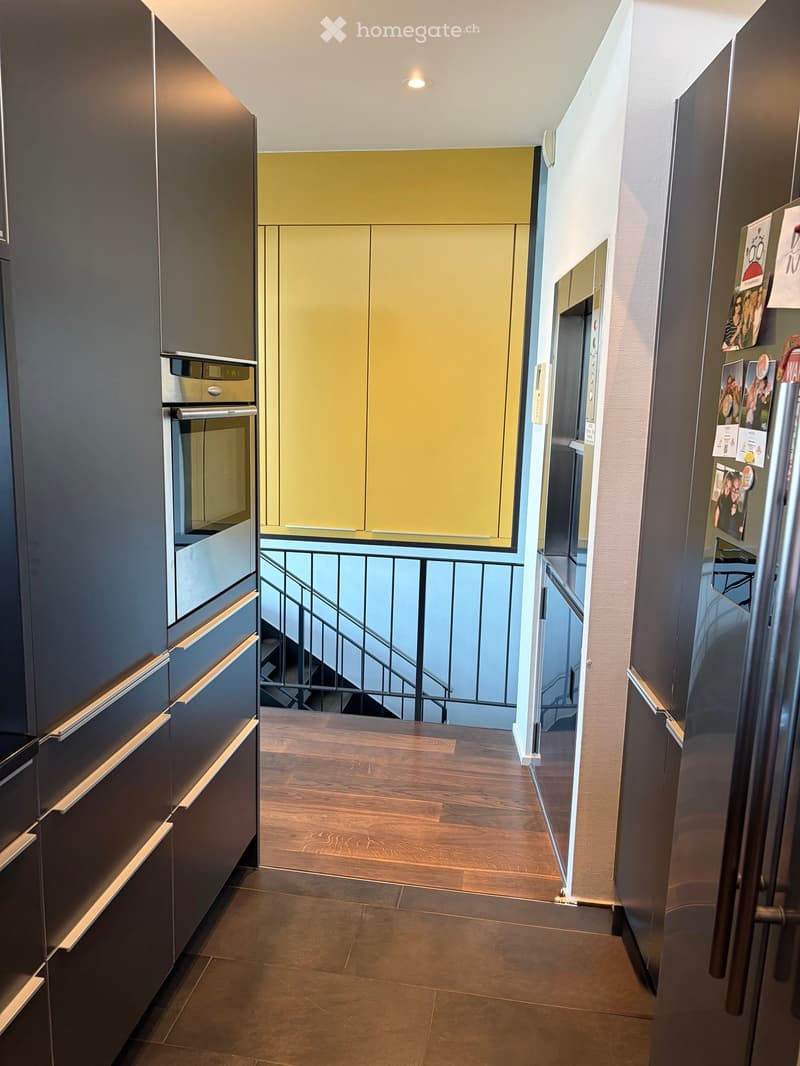 Modern hallway with wooden flooring, dark cabinets, and a staircase leading to a balcony area.