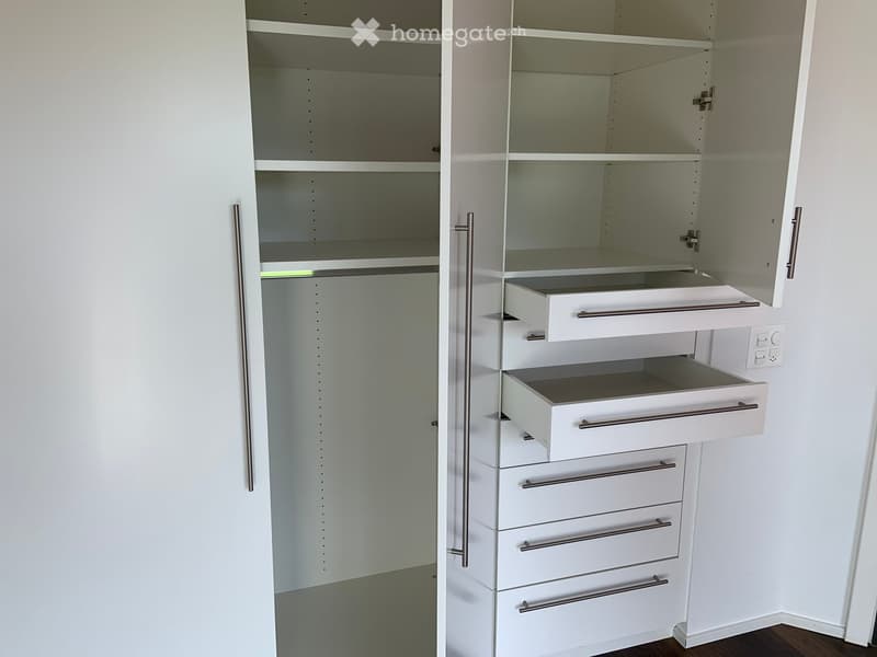 An empty closet with white built-in shelving and drawers, featuring multiple open compartments and closed drawers.