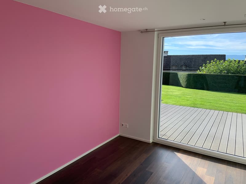 Empty room with wooden flooring, pink accent wall, and large sliding glass door leading to a wooden deck and garden.