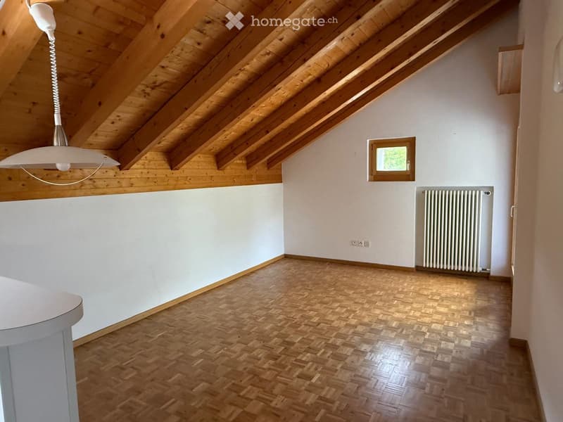 Empty attic room with wooden slanted ceilings, wooden flooring, white walls, a small window, and a radiator.