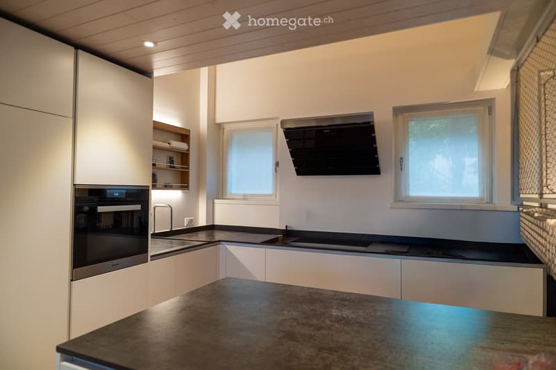 Modern kitchen with white cabinets, stainless steel appliances, and a dark countertop. Features include an oven, sink, and windows for natural light.