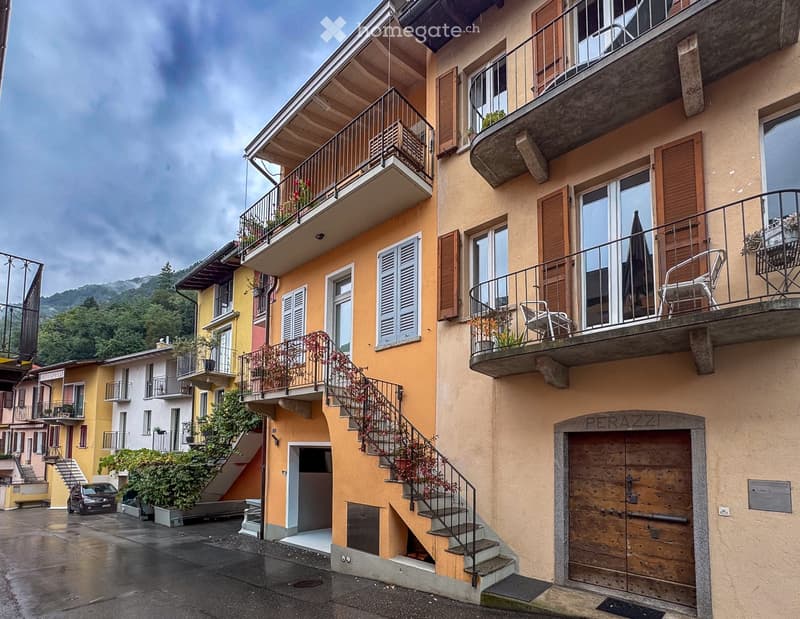 Multi-story residential building with balconies, wooden shutters, and a staircase leading to the entrance.