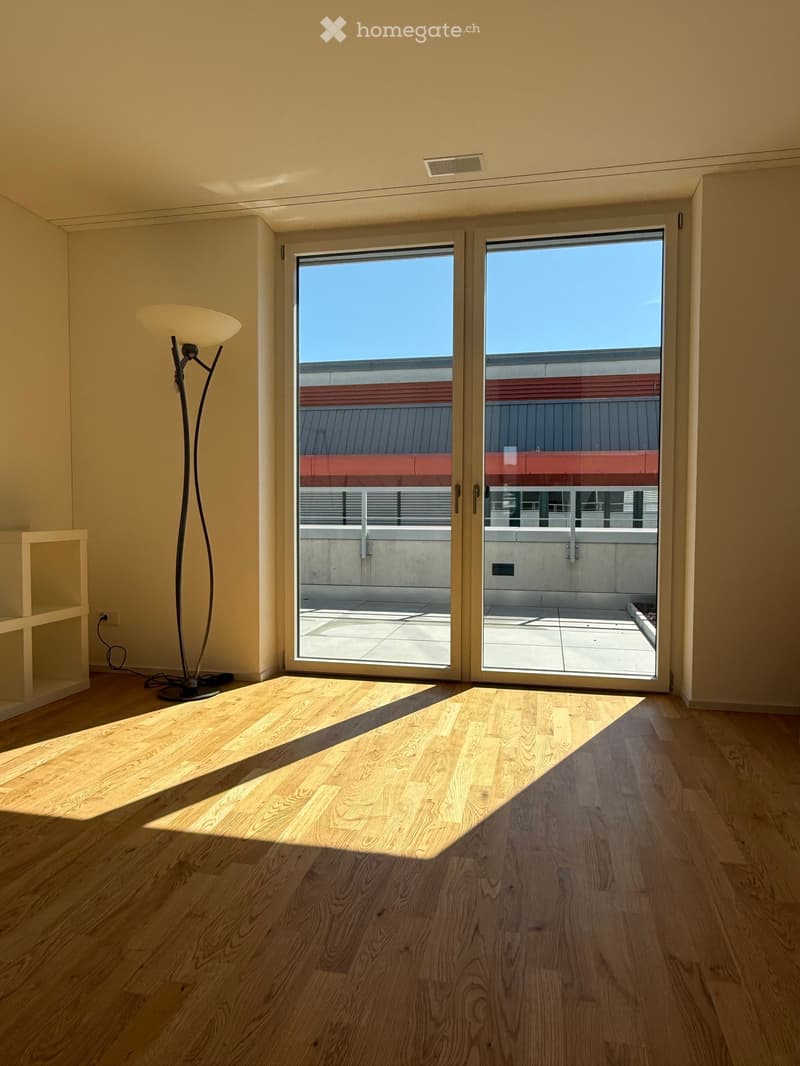Empty room with wooden flooring, large sliding glass doors leading to a balcony, and a modern floor lamp in the corner.