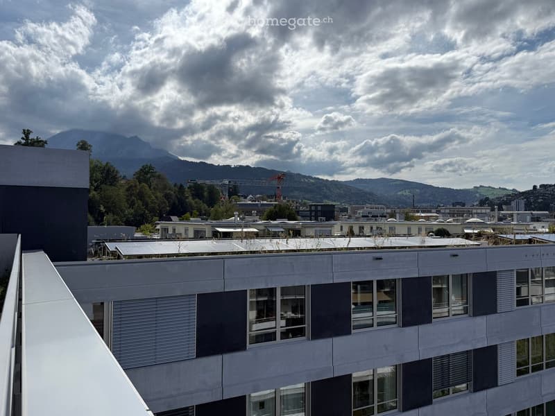 Modern multi-story building with large windows, solar panels on the roof, and a view of mountains and cityscape in the background.