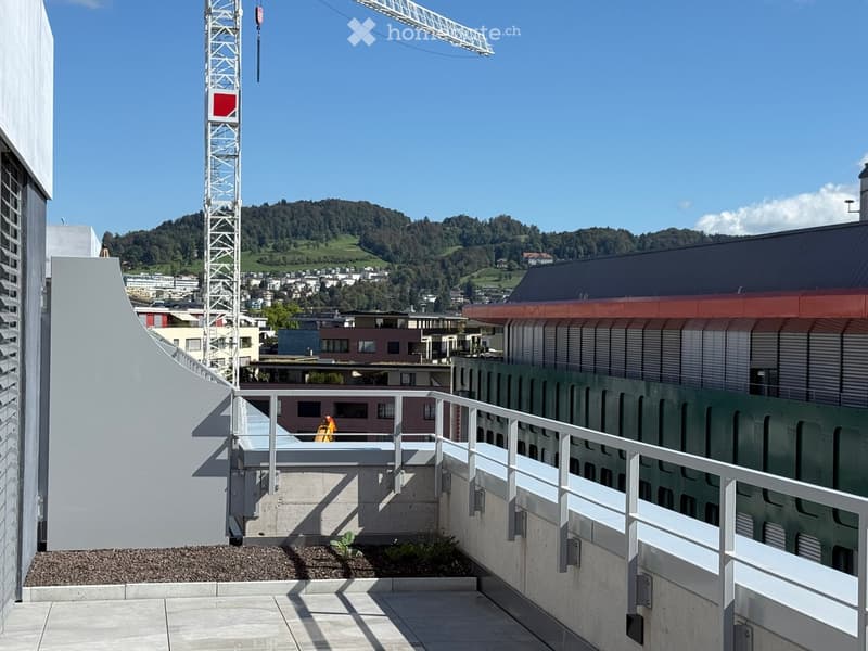 Balcony with white metal railing, concrete floor, and a view of a cityscape and mountains in the background.