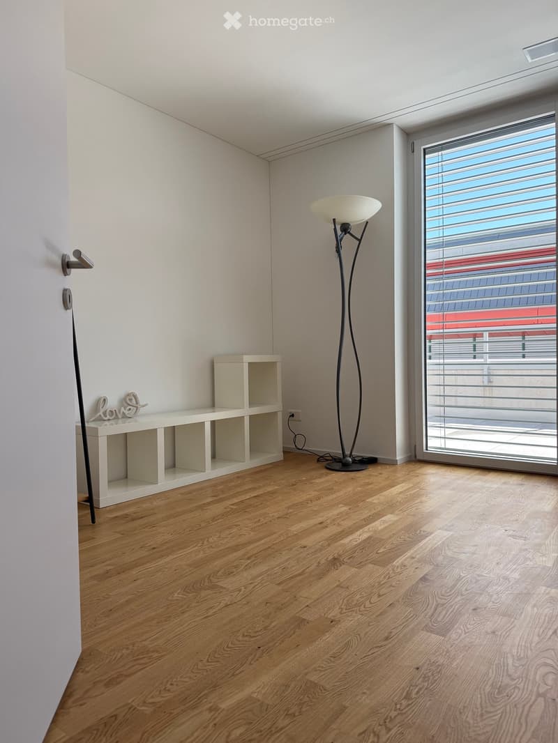 Minimalist room with light wooden flooring, white walls, a modern floor lamp, a small shelf, and a decorative 'love' sign.
