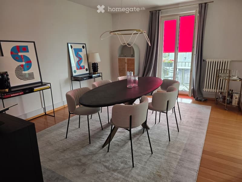 Dining room with a dark wooden table, six chairs, a modern lamp, and artwork on the walls. A sliding glass door leads to a balcony.