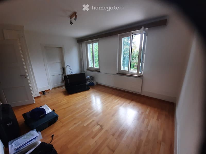 Empty room with wooden flooring, white walls, and large windows allowing natural light. No furniture or furnishings are present.