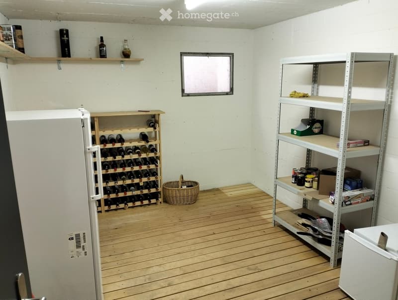 A small storage room with wooden flooring, white walls, and various storage items including a wine rack, shelves, and a basket.