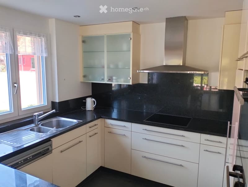 Modern kitchen with white cabinets, black countertops, stainless steel sink, electric kettle, and built-in oven.