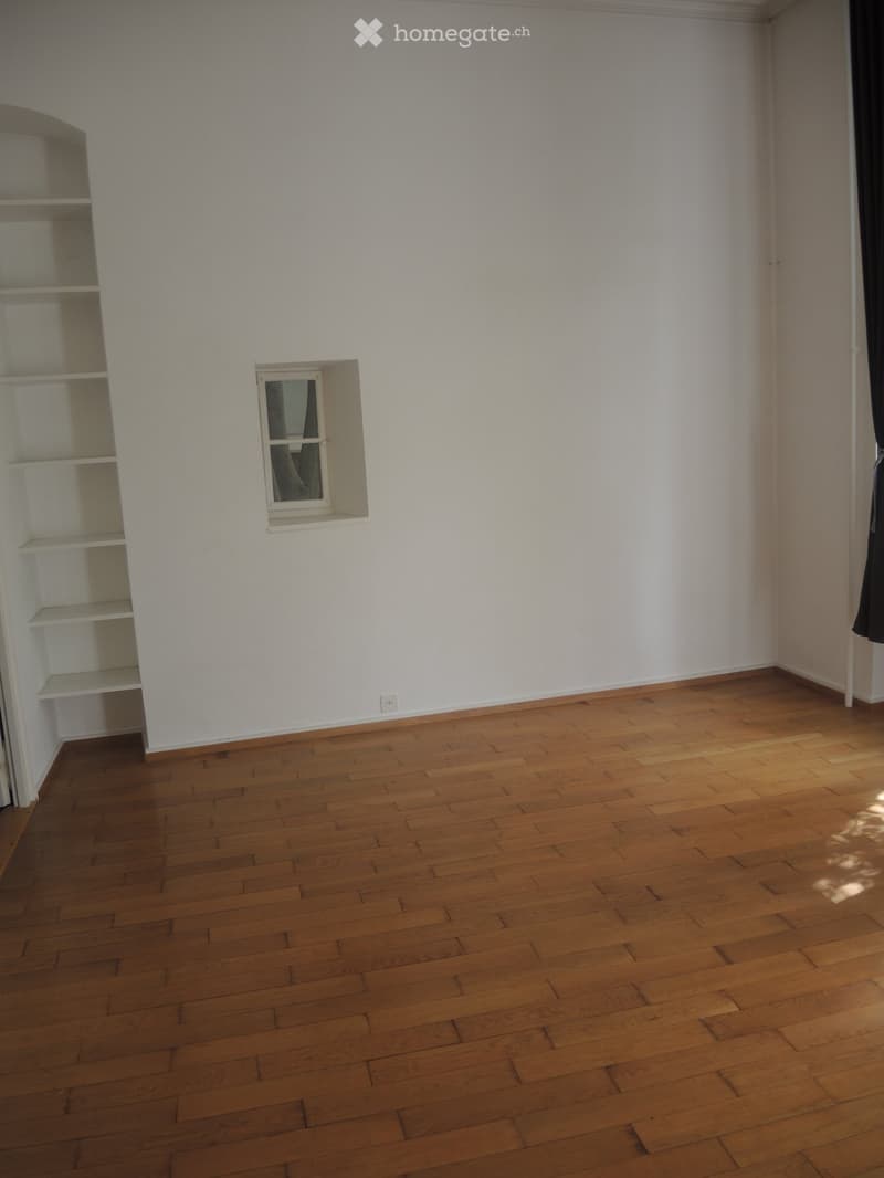 Empty room with white walls, wooden floor, window, shelves, outlet on the wall