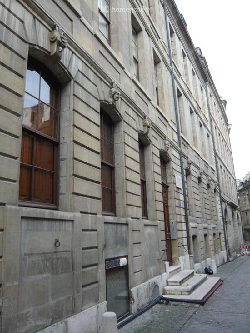 Gray stone facade, large arched windows, brown wooden windows, brown door, multiple floors, street-side view