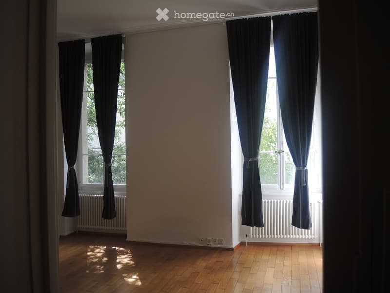 two large windows, black curtains, white walls, wooden floor, radiators