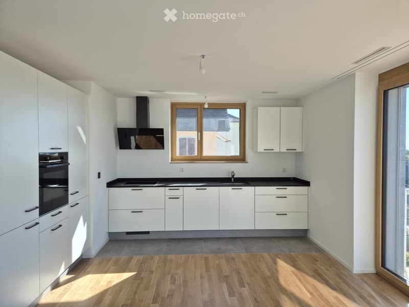 Modern kitchen with white cabinets, black countertops, and wooden flooring. Features a sink, oven, and range hood.