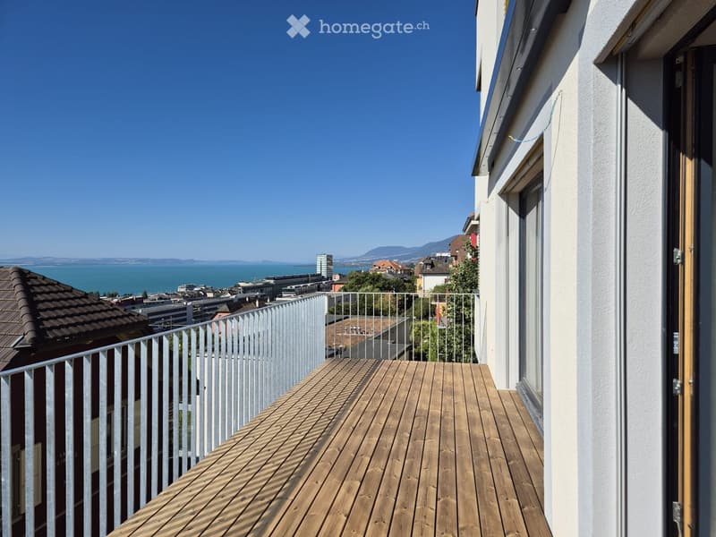 Balcony with wooden decking, metal railing, and scenic view of city and lake.