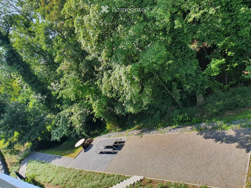 A gravel patio area with a picnic table and bench, surrounded by lush greenery and trees.