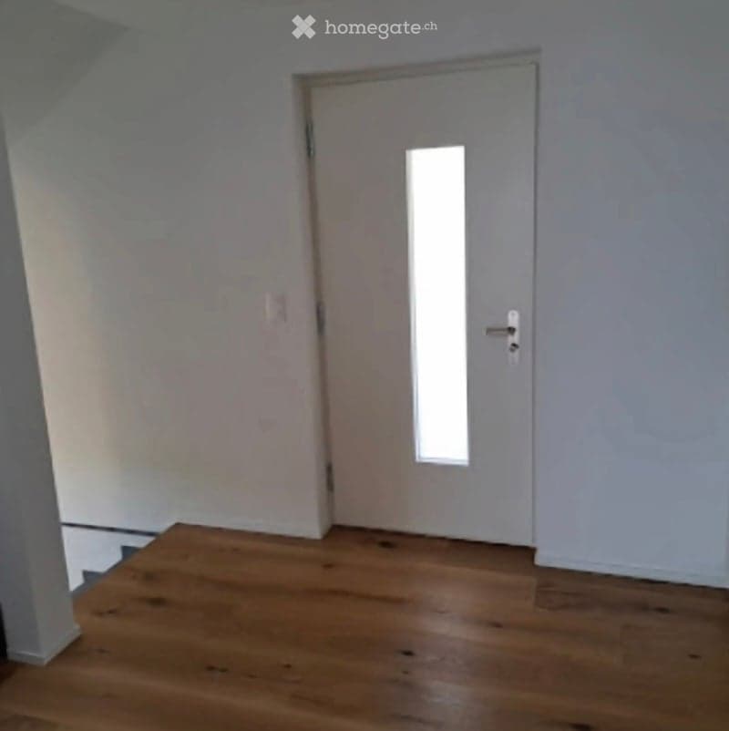 Empty room with wooden flooring and white walls, featuring a white door with a small window.
