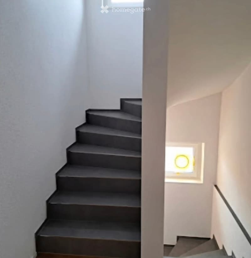 Modern interior staircase with dark grey steps and white walls, featuring a small window with a yellow circular design at the landing.