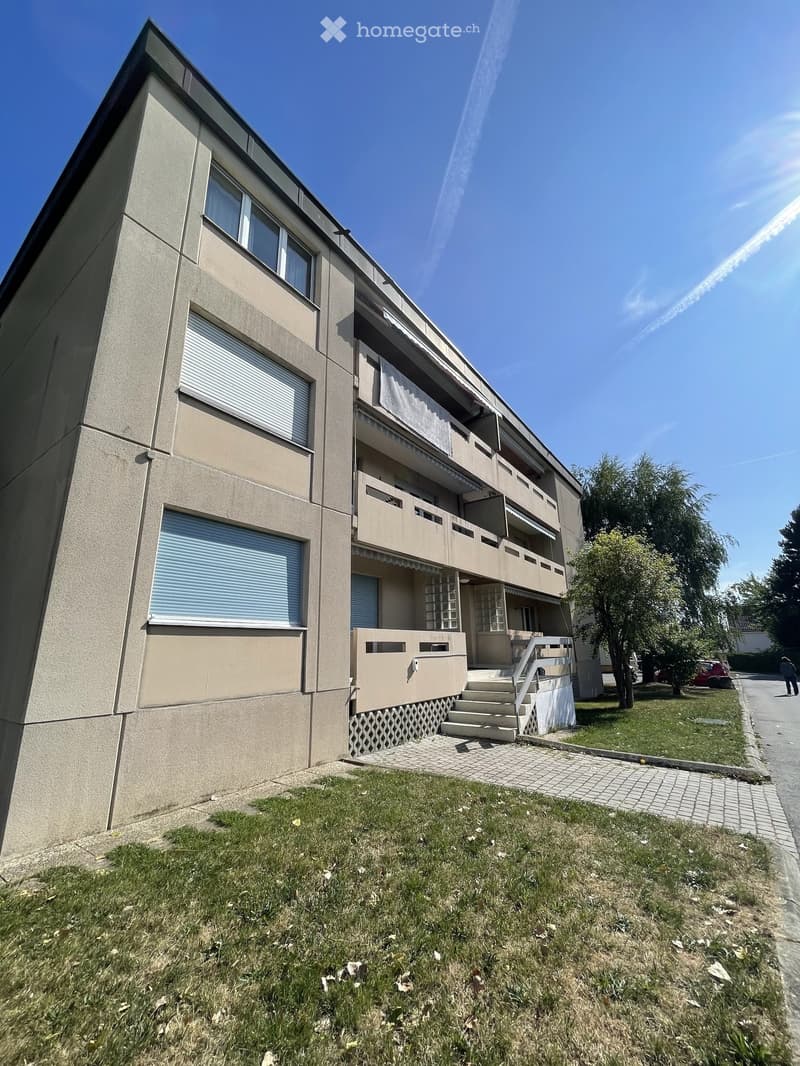 Four-story residential building with beige facade, multiple windows, balconies, and a staircase leading to the entrance.