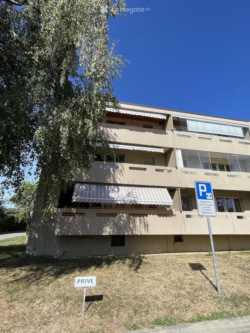 A three-story residential building with beige walls, multiple balconies, and striped awnings. A parking sign and a "PRIVE" sign are visible in the foreground.