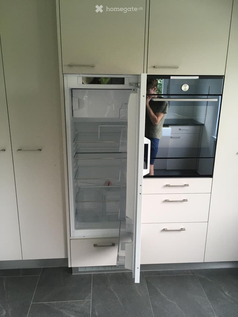 Modern kitchen with light-colored cabinets and an open refrigerator, showing empty shelves and drawers.