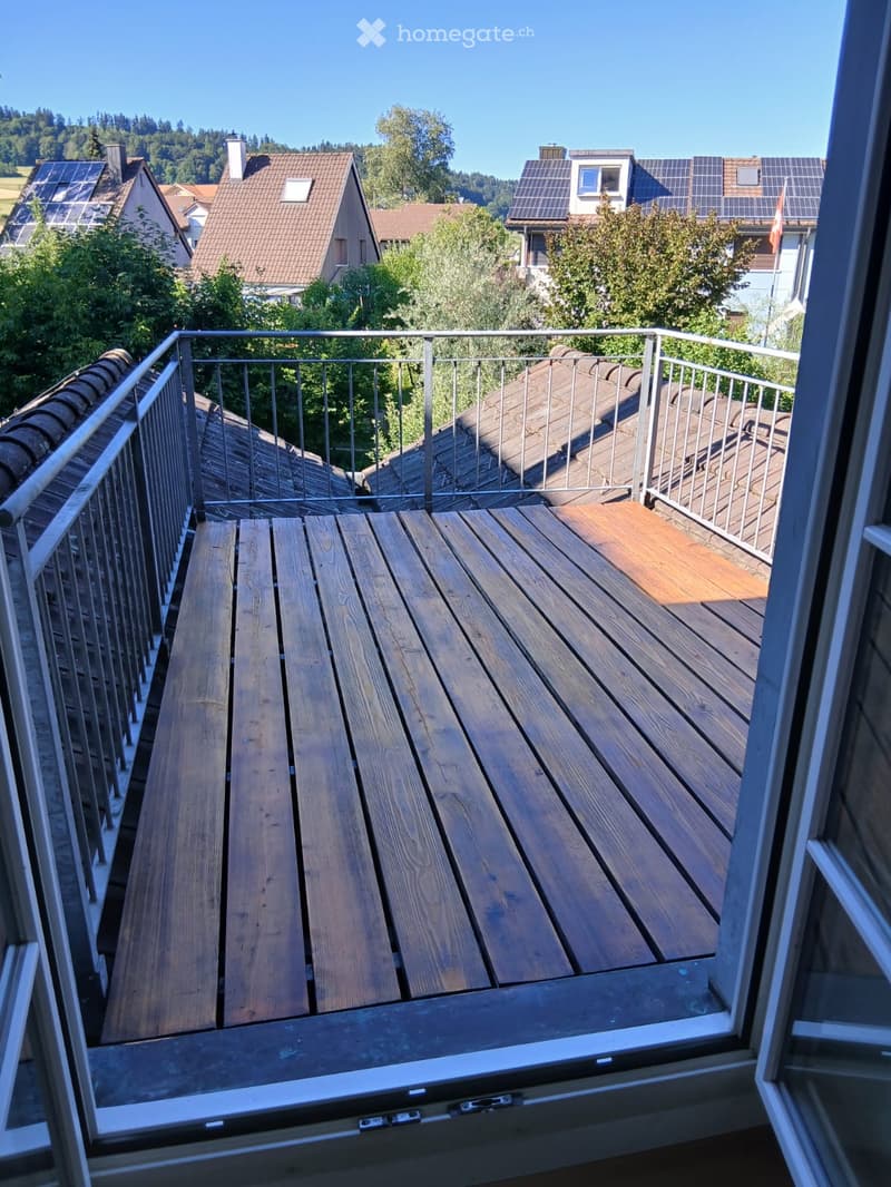 Wooden deck with metal railing, overlooking neighboring houses and rooftops.