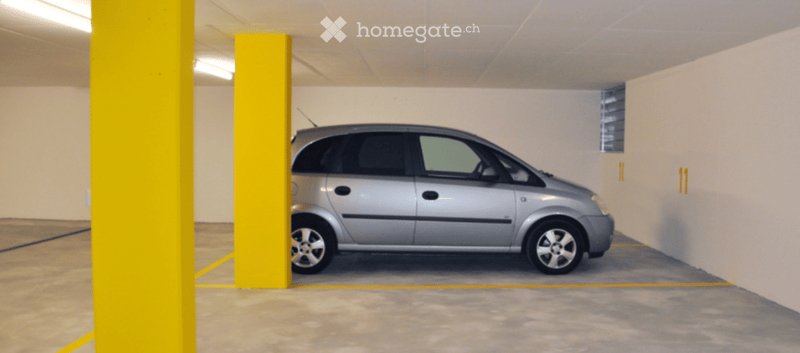 Underground parking area with a single silver car parked in a designated spot, surrounded by yellow pillars and marked parking lines.