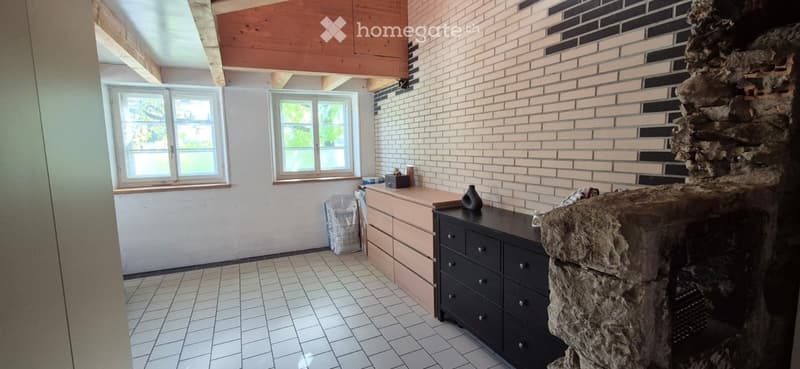 Bright room with exposed wooden beams, white tiled floor, and a stone fireplace. Includes a dark wooden cabinet, a vase on the mantel, and a drawer unit.