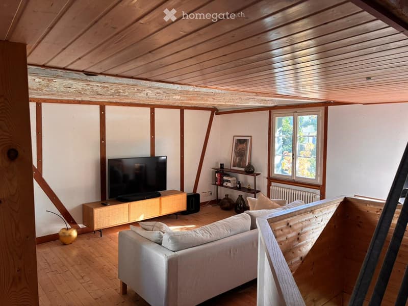 Living room with wooden ceiling and floor, white walls, large window, grey sofa, coffee table, television, bookshelf, and decorative vases.