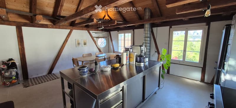 Open-concept kitchen with stainless steel counter, coffee maker, fridge, dining table, chairs, and decorative items.
