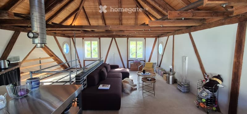 Open-concept living space with exposed wooden beams, a sectional sofa, coffee table, side tables, and a dog resting on the floor.