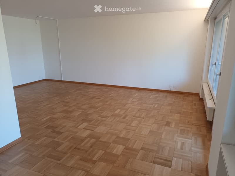 Empty room with wooden parquet flooring and white walls, featuring a window and radiator on one side.