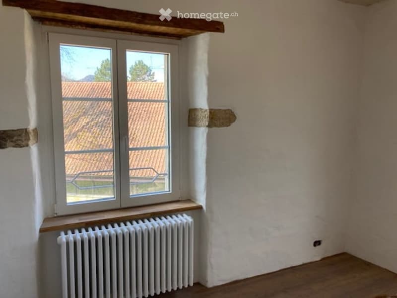 Empty room with white walls, wooden floor, white radiator, window with wooden frame