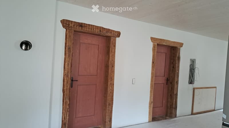 An empty room with two wooden framed doors and white walls. There is a light switch on the wall between the doors.