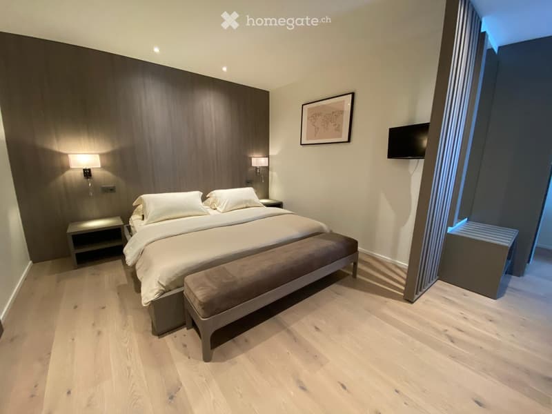 Large bedroom with a double bed, two nightstands, a wall-mounted flatscreen television, a picture frame, and a bench.