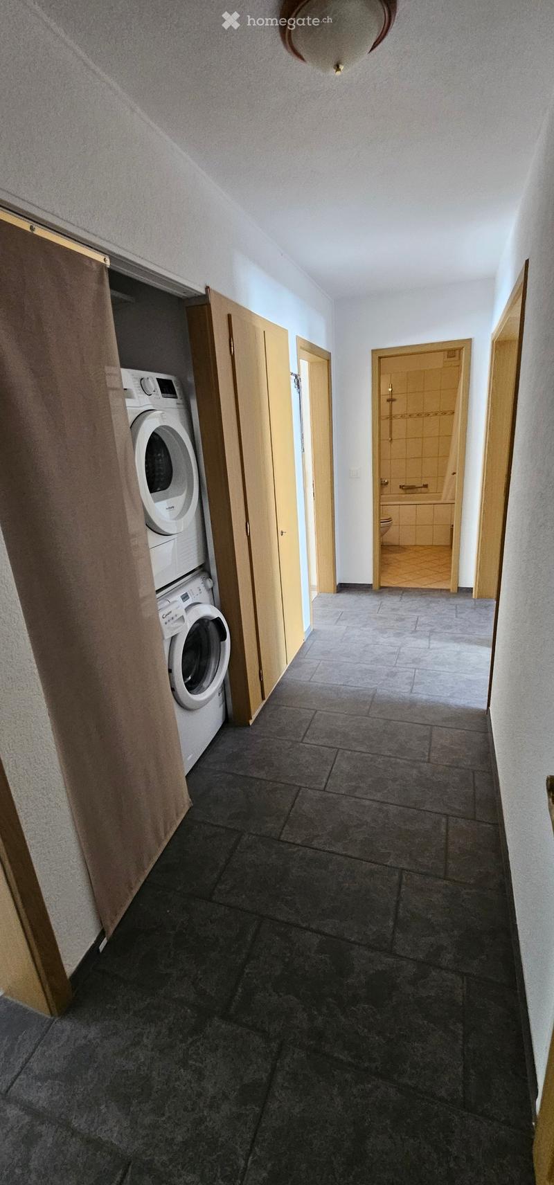 Hallway with dark tiled floor, wooden doors, and a washing machine in a closet on the left side.