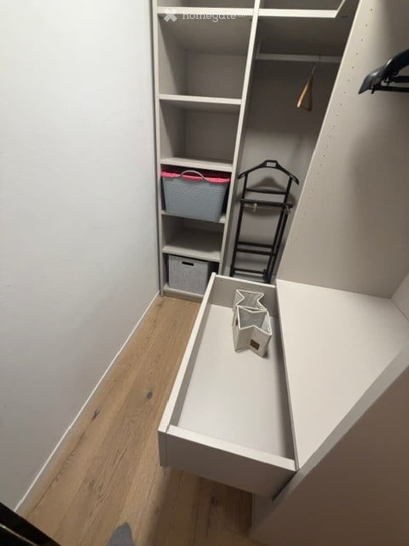 Empty walk-in closet with built-in shelving units, wooden floor, and a small bench with decorative items.