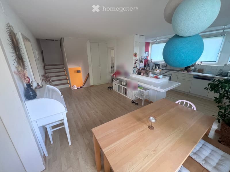 Open-plan living and dining area with wooden flooring, white kitchen island, dining table, chairs, and a staircase leading to another level.