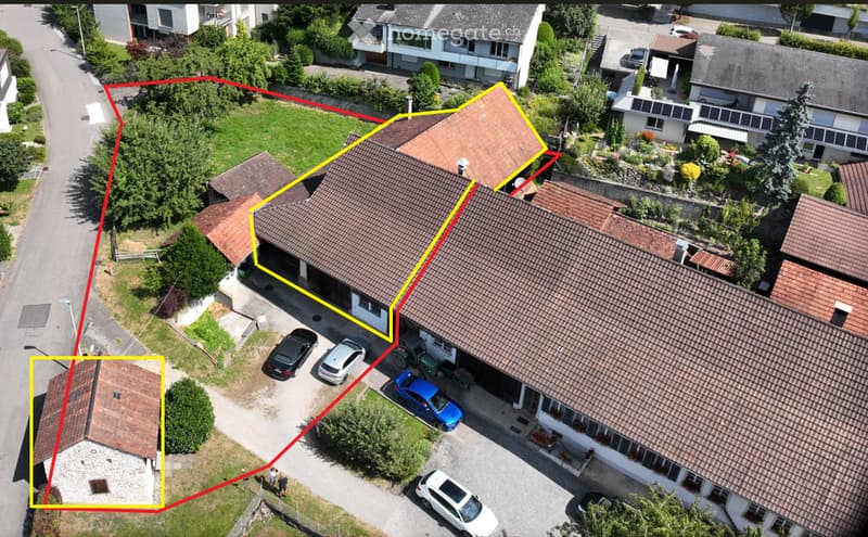 Aerial view of a residential building with a garage, multiple parked cars, and surrounding greenery.