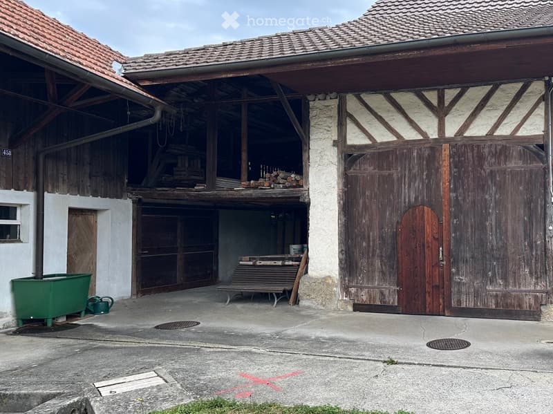 A rustic wooden barn with a tiled roof, large wooden doors, and a partially open side revealing stored materials and tools.