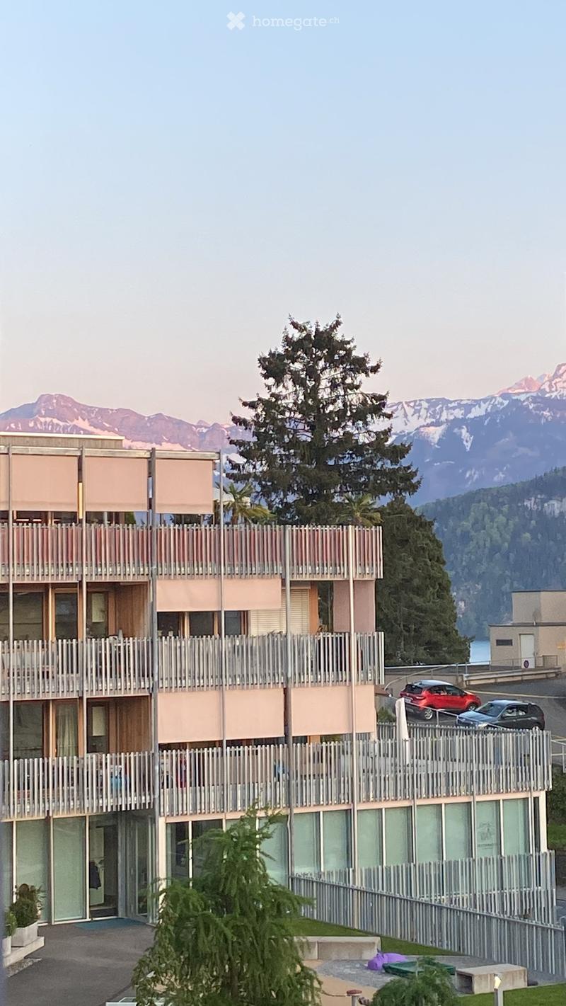 Modern multi-story building with balconies overlooking a scenic lake and mountain backdrop.