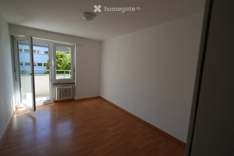 Empty room with wooden flooring, white walls, and large windows leading to a balcony. No furniture or equipment is present.