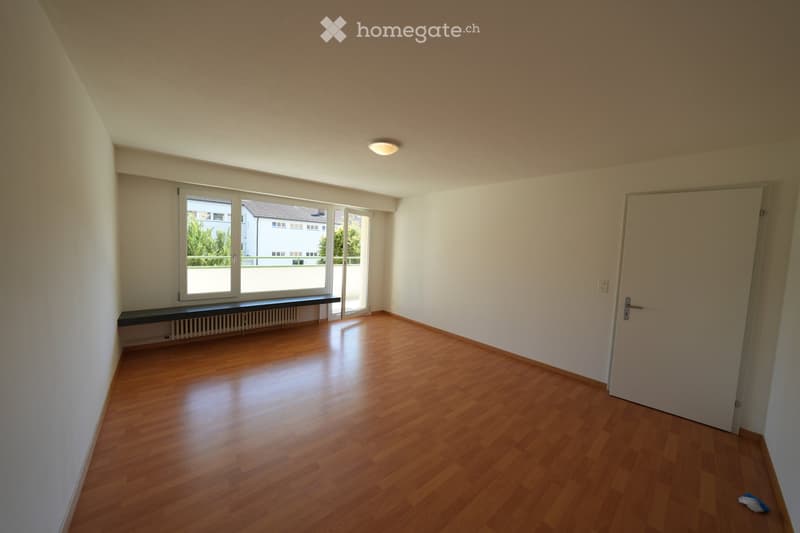 Empty room with wooden flooring, white walls, large window with view, and a door.