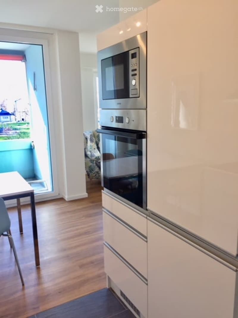 Kitchen with built-in appliances, open sliding door to balcony, wooden floor, dining table and chairs