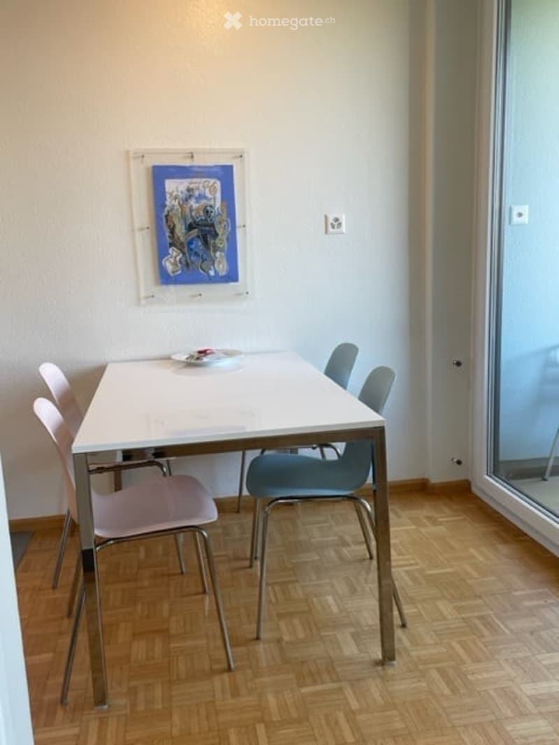 Dining room with a white table and pink and blue chairs. A painting is on the wall.
