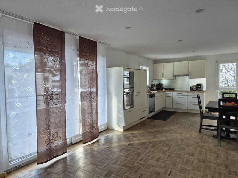 Modern kitchen with white cabinets, stainless steel appliances, wooden flooring, and a dining area with a table and chairs.