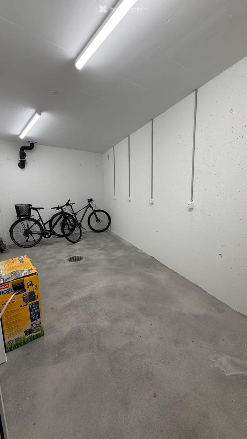 Empty garage with concrete floor, white walls, fluorescent lighting, and two bicycles stored against the wall.