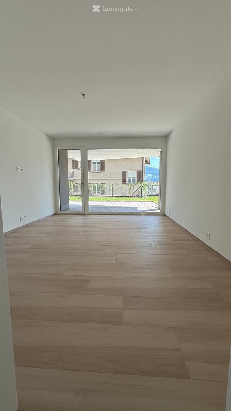 Empty room with light wooden flooring and white walls, featuring large glass sliding doors leading to an outdoor area.