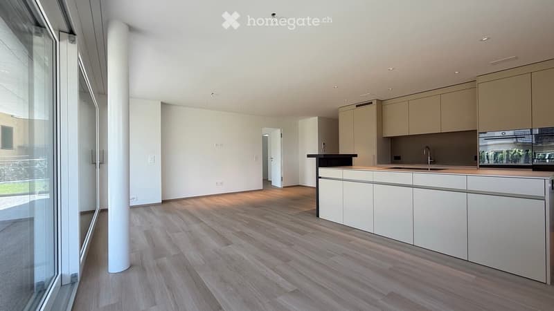 Modern kitchen with light-colored cabinets, a central island, and a sleek countertop. The space features wooden flooring and large windows that allow natural light to fill the room.